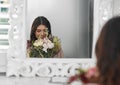 This is going to be an amazing day. a beautiful woman smelling flowers while sitting in front of the mirror.