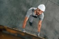 Going up on the ladder, top view. Young factory worker in grey uniform