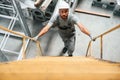 Going up on the ladder, top view. Young factory worker in grey uniform