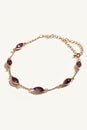 A gold ankle bracelet featuring oval-cut amethysts in a bezel setting, laid against a white background