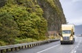 Gold big rig semi truck transporting cargo in refrigerator semi trailer driving on the wet mountain road with rock cliff on the Royalty Free Stock Photo