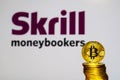 Gold Bitcoin coins with the Skrill logo on background screen.