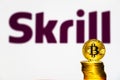 Gold Bitcoin coins with the Skrill logo on background screen.