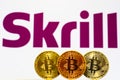 Gold Bitcoin coins with the Skrill logo on background screen.