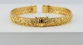 A gold bracelet with intricate filigree detailing sits on a white surface. Featuring Royalty Free Stock Photo