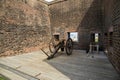 A gold and brown cannon surrounded by the red brick walls of a military fort on a brown wooden floor at Old Fort Jackson in