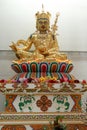 A gold Buddhist Guru Rinpoche Padmasambhava statue sitting on a colourful pedestal