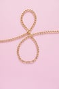 A gold chain laid out in the shape of a eight on a pink background Royalty Free Stock Photo