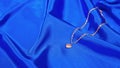 Gold chain with a pendant in the form of a heart on a blue satin background. Luxury women`s jewelry, close-up Royalty Free Stock Photo