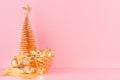 Gold christmas tree with glowing stars lights, balls in bowl, present on elegant pastel pink background. Royalty Free Stock Photo
