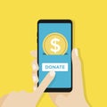 Gold coin and donate button on smartphone screen. Hand holds smartphone, finger touches screen.