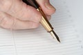 Gold coloured fountain ink pen in senior woman hand about to write something on empty daily planner page, closeup detail