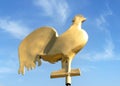 Gold coloured village church steeple cockerel weather vane with beautiful clear blue summer sky behind. Bright golden gilded.