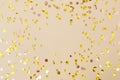 Gold confetti on beige paper background. Festive holiday backdrop. Birthday congratulations Christmas New Year.