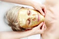 Gold cosmetic mask, the beautician applies a gold mask to a woman`s face.