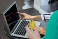 Gold credit card in the hand of a woman in a green dress. Her friend pointing finger at laptop computer screen in the background Royalty Free Stock Photo