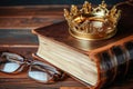 gold crown on a leatherbound book with glasses beside