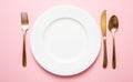 Gold cutlery and dishes set against pink background, formal place setting Royalty Free Stock Photo