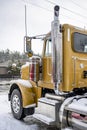 Gold day cab bonnet big rig semi truck tractor standing on the winter industrial warehouse parking lot with snow and ice Royalty Free Stock Photo