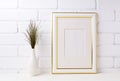 Gold decorated frame mockup with dark grass in vase near brick w