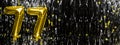 Gold foil balloon number number 77 on a background of black tinsel decoration. Birthday greeting card, inscription