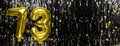 Gold foil balloon number number 73 on a background of black tinsel decoration. Birthday greeting card, inscription