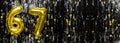 Gold foil balloon number number 67 on a background of black tinsel decoration. Birthday greeting card, inscription sixty