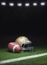 A gold football helmet and football on a grass field with stripe on dark background with stadium lights Royalty Free Stock Photo