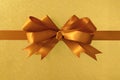 Gold gift bow ribbon, shiny metallic foil paper background, horizontal