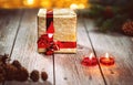 Gold gift box and pine branch with cones with candles on wooden table. Background bokeh yellow lights. Royalty Free Stock Photo