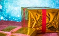 Gold gift box with red ribbon, on Christmas sparkling blue background Royalty Free Stock Photo