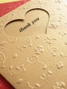 Gold greeting card pierced into a heart shape inside with the word `thank you` and pattern a small flower shape over red paper. Royalty Free Stock Photo