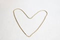 A gold heart is made of chain, symbol of love on a white textural background