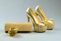 Gold high-heeled shoes, clutch bag and perfume on a gray backgr