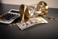 Gold hourglass with hundred us dollars banknotes and calculator with coins isolated on grey table Royalty Free Stock Photo