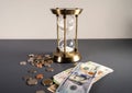 Gold hourglass with hundred us dollars banknotes with coins isolated on grey table Royalty Free Stock Photo