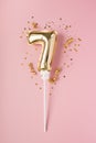 Gold inflatable number 7 on a stick with gold confetti on a pink background