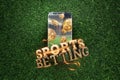 Gold inscription Sports Betting on a smartphone on a background of green grass. Bets, sports betting, bookmaker. Mixed media Royalty Free Stock Photo