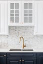 A gold kitchen sink surrounded by white and blue cabinets and a marble backsplash. Royalty Free Stock Photo
