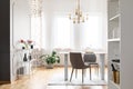 Gold lamp above table and chairs in bright dining room interior with flowers and windows. Real photo Royalty Free Stock Photo