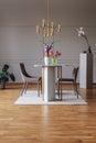 Gold lamp above table with flowers in spacious grey dining room interior with chairs. Real photo