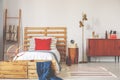 Gold lamp between wooden cabinet and bed with red cushion in sport bedroom interior. Real photo Royalty Free Stock Photo