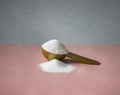 Gold measuring spoon with collagen on pastel pink gray background. Powdered hydrolyzed fish collagen supplement.
