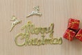 Gold Merry Christmas text and Red Gift Box on a brown wooden flo