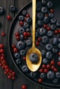 The gold metal spoon, black wood desk surface and fresh natural berries: blueberries and red currant on dish on a table Royalty Free Stock Photo