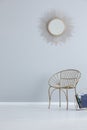 Gold mirror on grey empty wall above armchair in simple hall interior with copy space