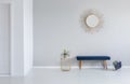 Gold mirror on the wall above blue bench in minimal empty entrance hall interior with plant