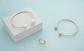 Gold and pearl bracelets and modern ring on white cube on blue background