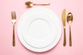 Gold cutlery and dishes set against pink background, formal place setting Royalty Free Stock Photo
