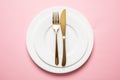 Gold cutlery and dishes set against pink background, formal place setting Royalty Free Stock Photo